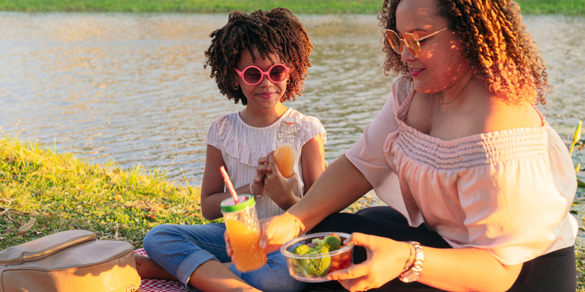 A mother and daughter enjoy a lakeside picnic that features fresh vegetables.