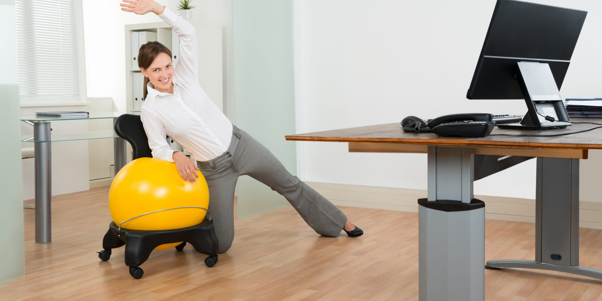 Woman uses exercise ball for stretches in her office where she also has a standing desk.