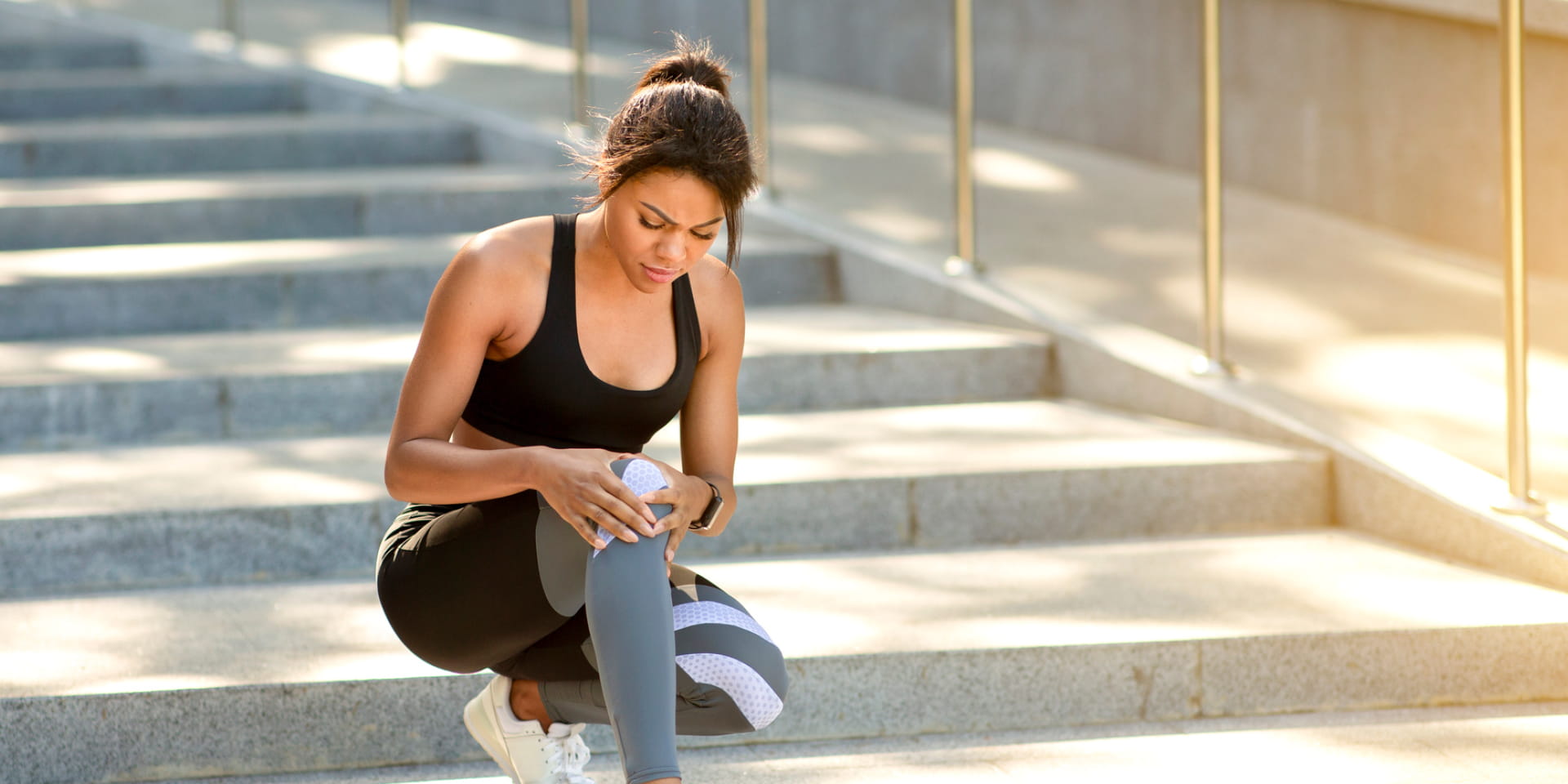 Young woman seated on steps grasping her knee.