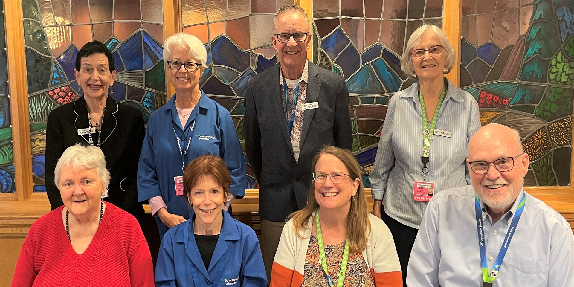 A group of Doylestown Hospital's volunteer chaplains gather in front of the stained glass windows of the hospital's Mary and Gerald Santucci Chapel.