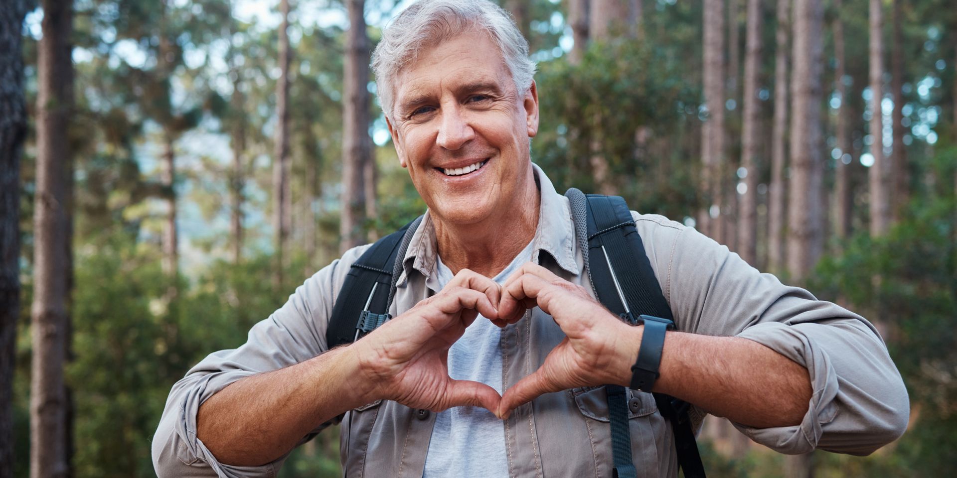 Man hiking in woods making heart sign with his hands.